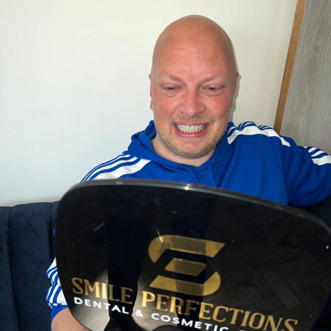 patient smiling, holding a mirror looking at this teeth after getting teeth in a day treatment in Leicester