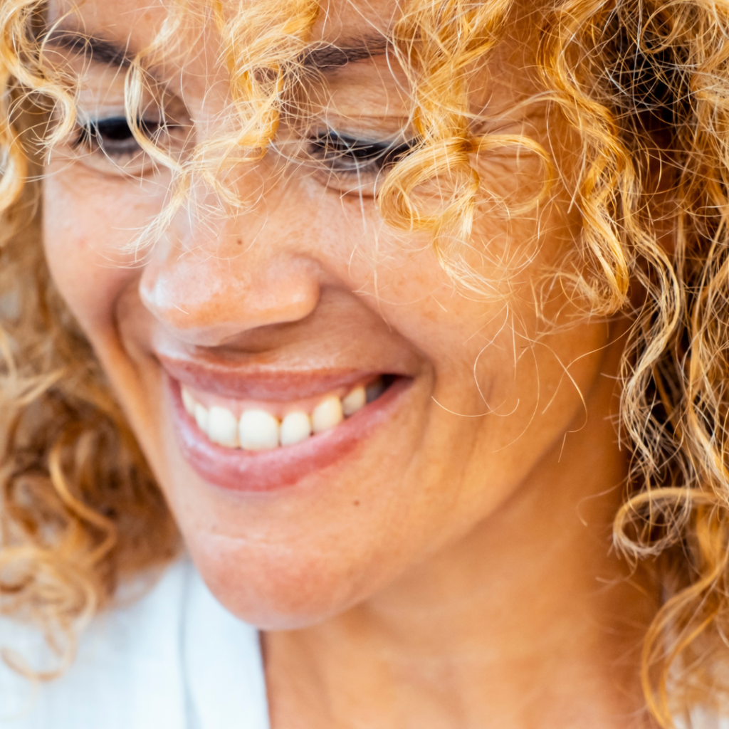close-up of a young woman, smiling, looking down representing the photo for dental bridge in Leicester
