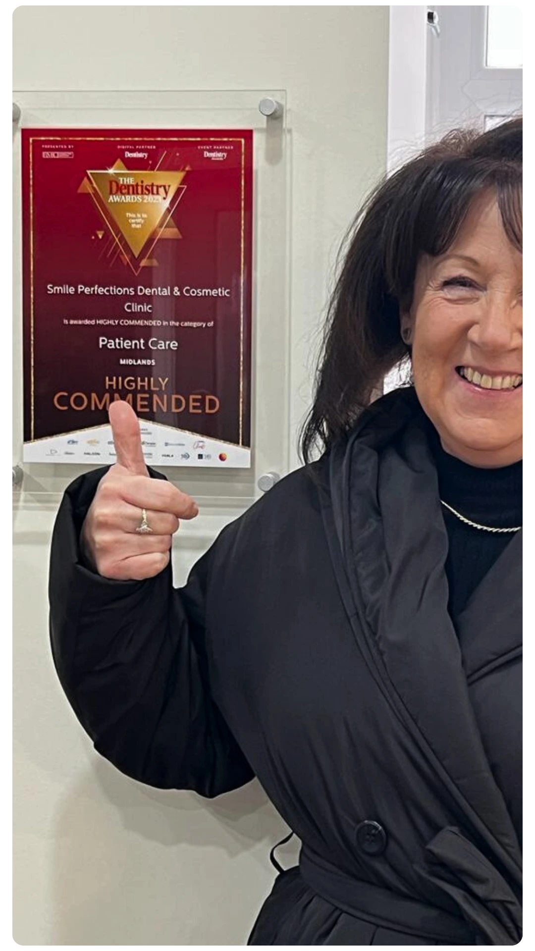 Woman smiling and giving a thumbs up next to the “Patient Care” award at Smile Perfections in Leicester, celebrating recognition for outstanding dental service.