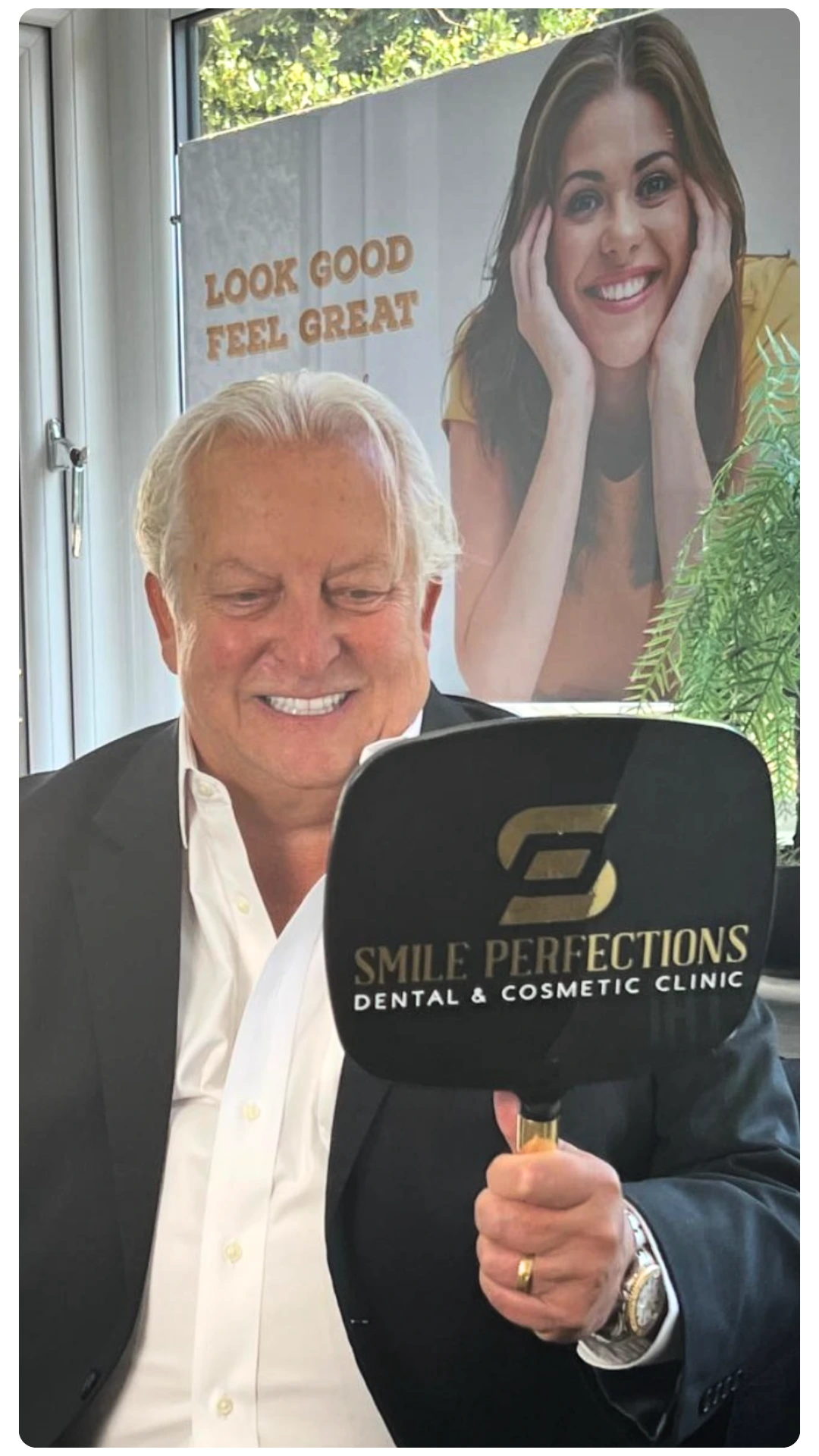 Slightly older male looking at his smile in the mirror after receiving dental treatment at Smile Perfections showing a positive experience
