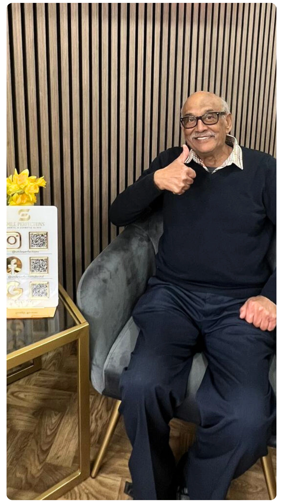 Slightly older male patient sitting in an armchair at the reception of Smile Perfections in Leicester, smiling and giving a thumbs up after a positive dental experience.