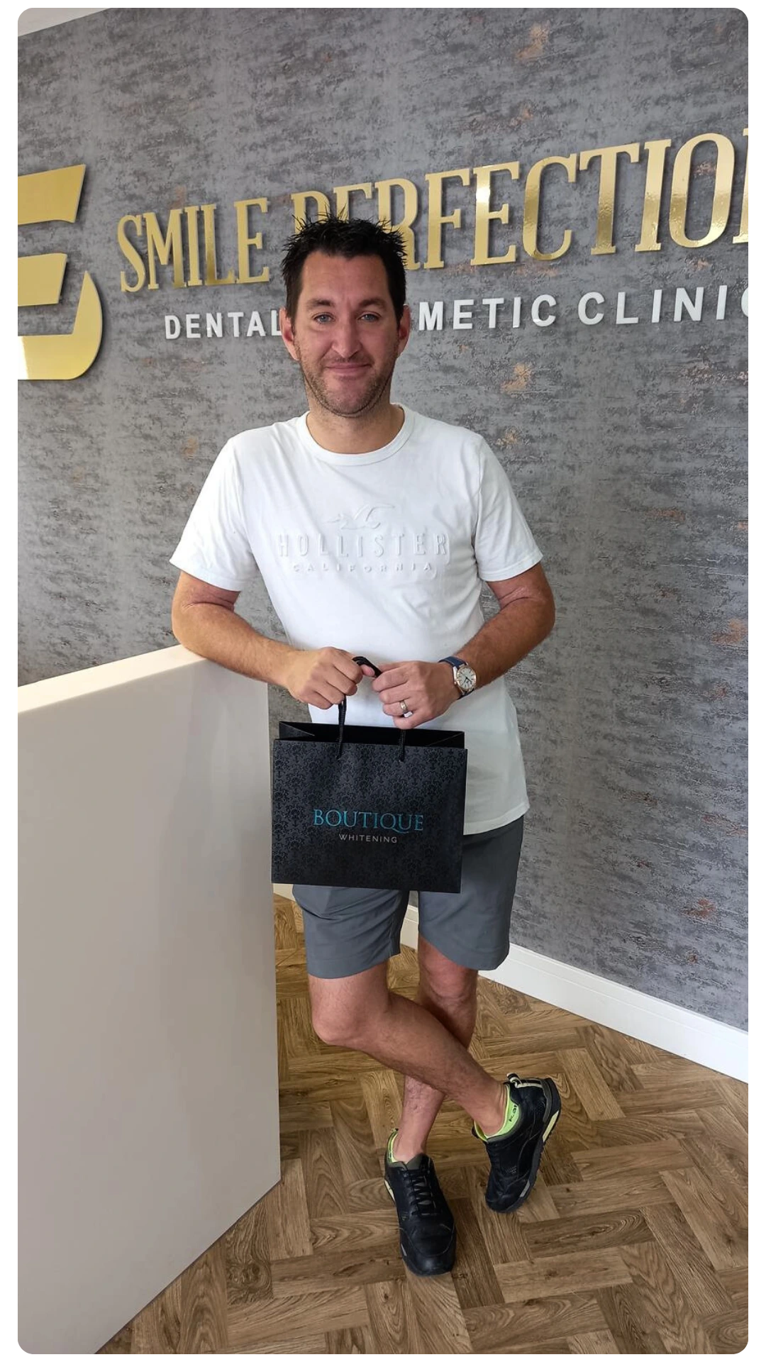 Male patient smiling at the reception of Smile Perfections in Leicester, posing with a Boutique Whitening bag in hand after receiving professional teeth whitening treatment.